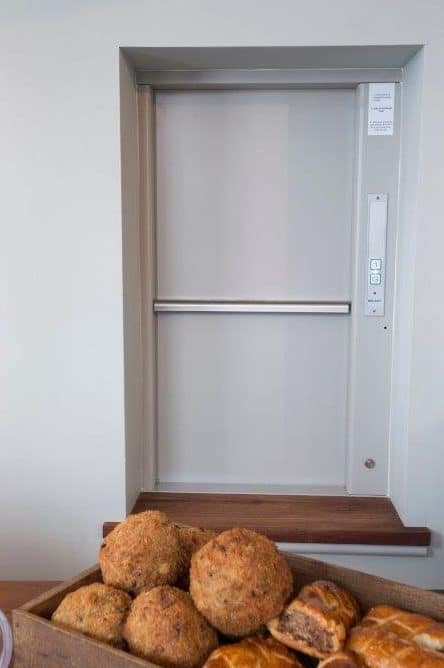 a gartec dumbwaiter with a box of fresh bread rolls in front of it