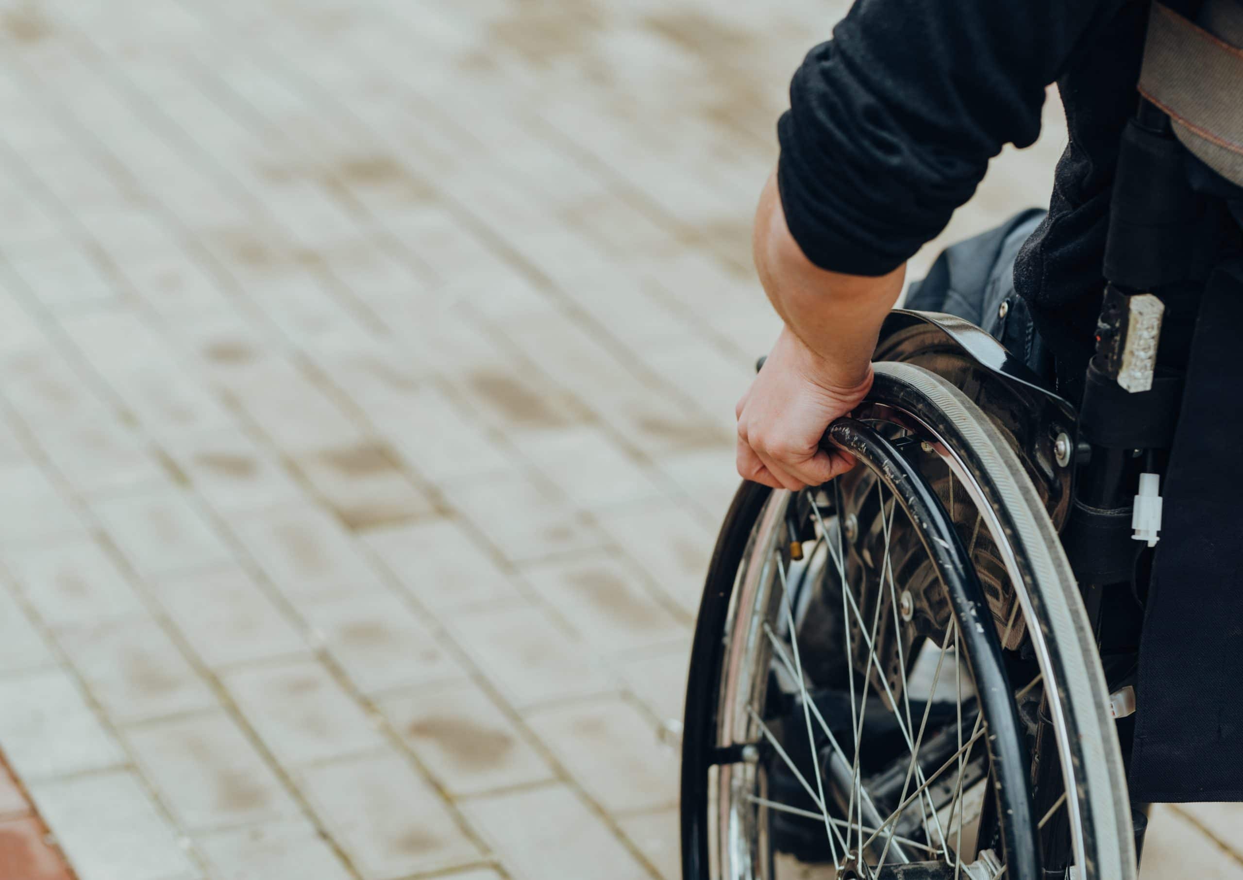 Close-up of male hand on wheel of wheelchair during walk in park. He holds his hands on the wheel.