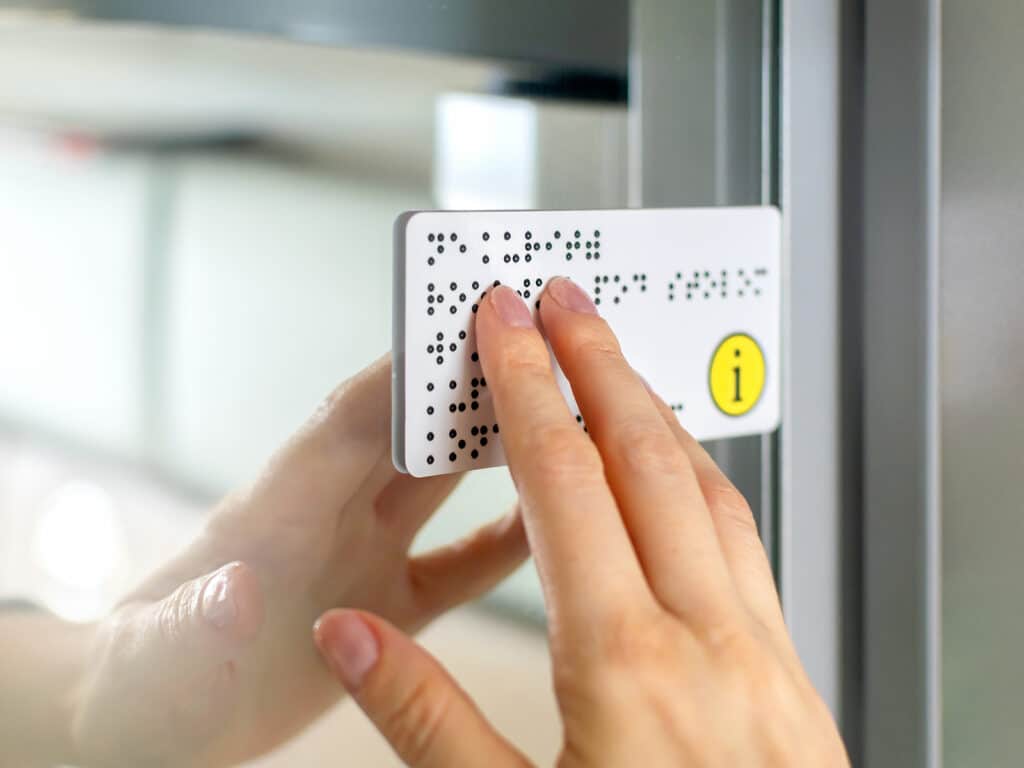 Close-up of fingers touching a braille notice on a door