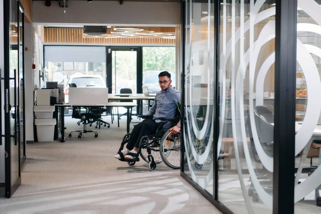 In a large modern corporation, a determined businessman in a wheelchair navigates through a hallway, embodying empowerment and inclusivity in the corporate world.