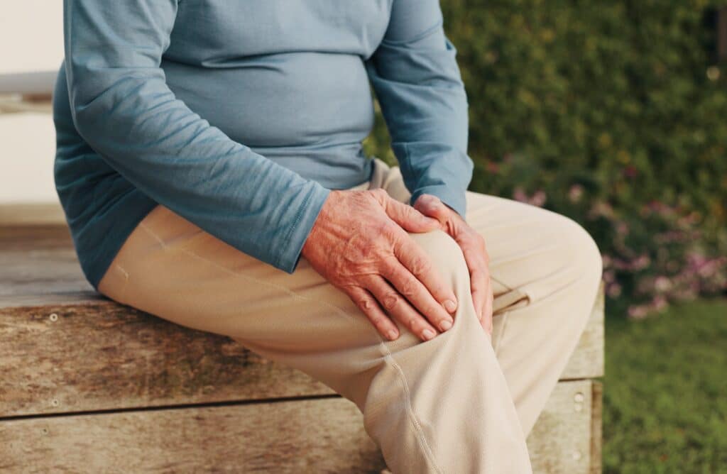 Knee pain, hands and backyard with old man in home for osteoarthritis, injury and joint issue. Fibromyalgia inflammation, fracture risk and pressure with senior person outdoor for tension and sprain