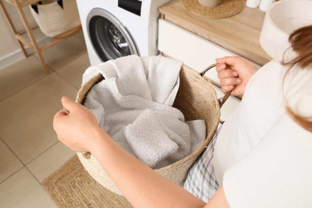 Woman carrying a laundry basket filled with clean white towels in a modern home laundry room, Daily household chores and the routine of washing and caring for textiles